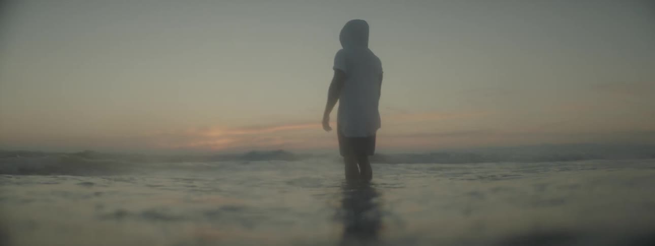 A man wades in ocean water at sunset