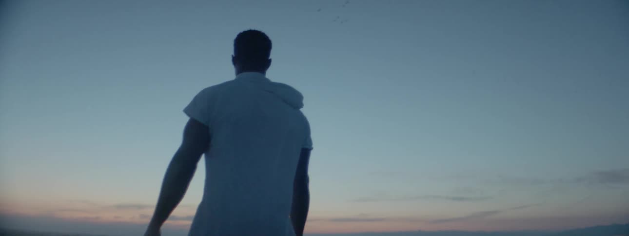 A man in a white shirt is standing looking at the sunset