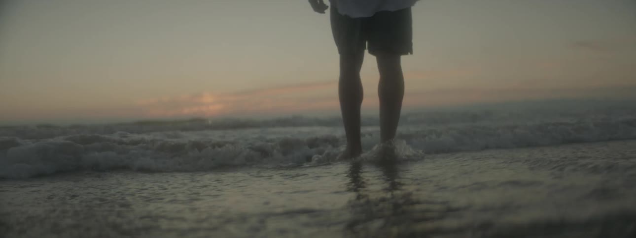 A man wades in ocean water at sunset