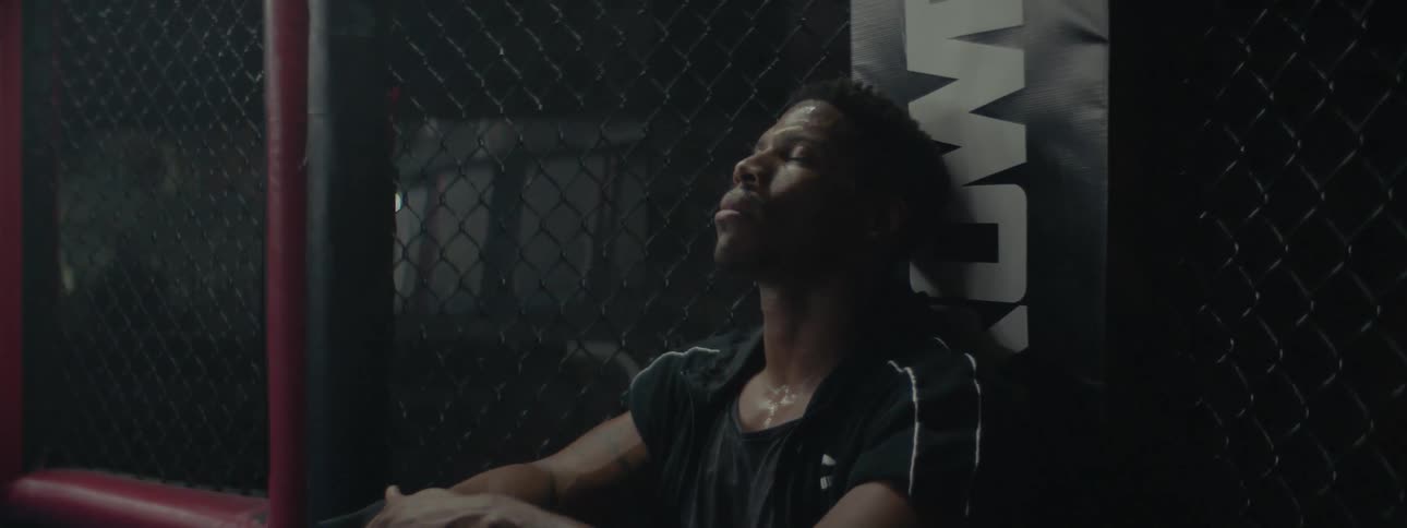 A man is sitting up against the corner in a mma fighting cage