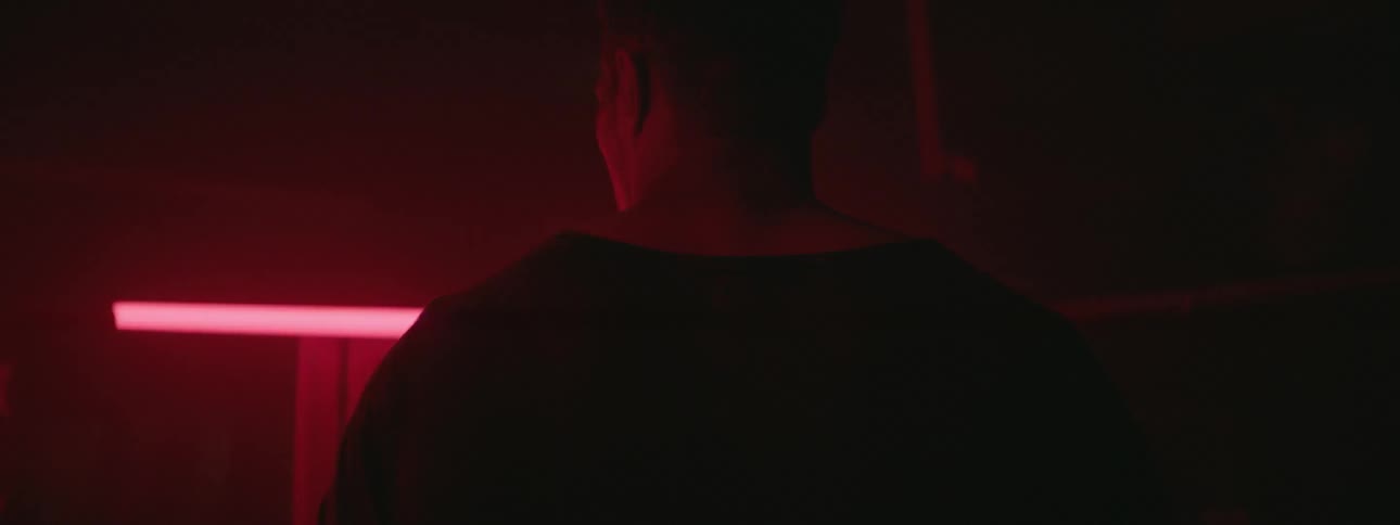 A man in a sweatshirt stands in a red lit room
