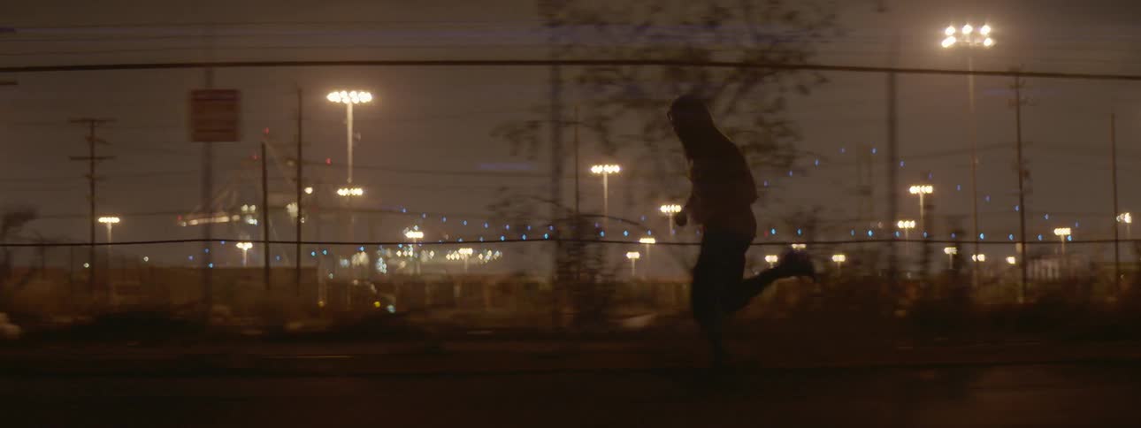 A man jogs on a fenced sidewalk at night