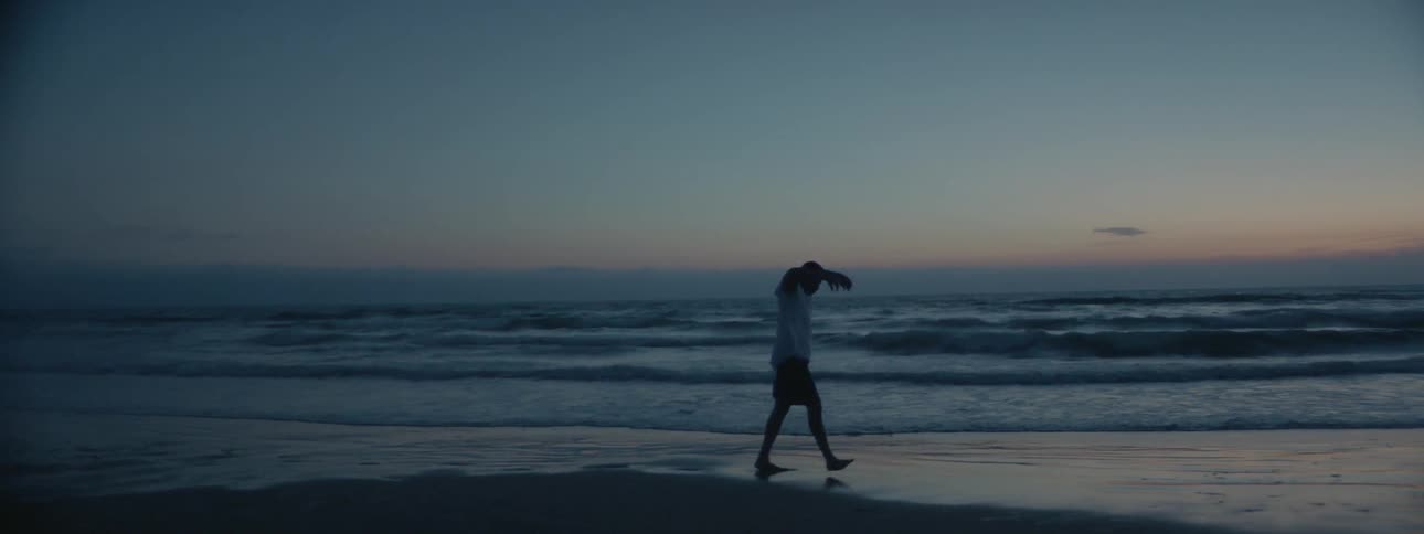 A man paces and flails his arms on the beach at sunset