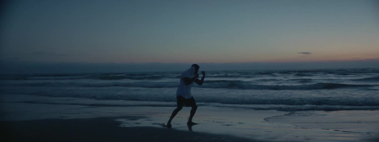 A man shadow boxes and kicks outside by the water