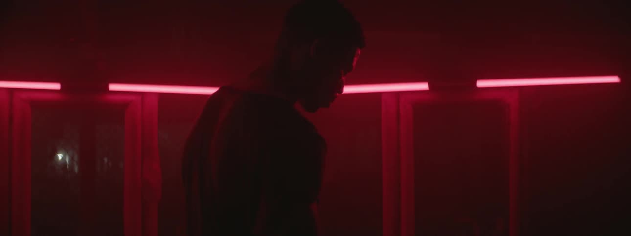 A man stands in a room lit by red neon lights