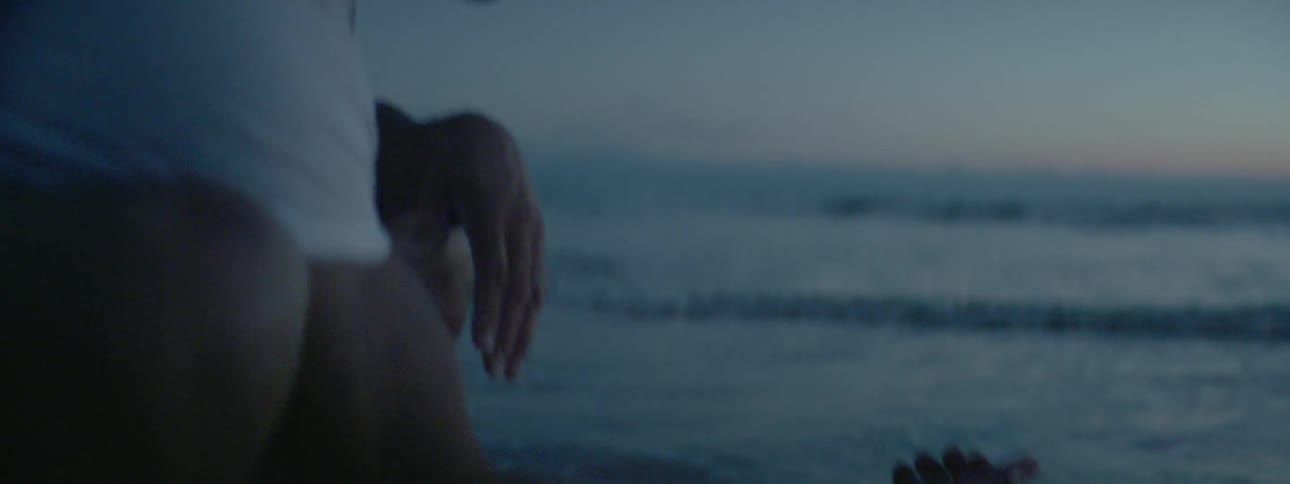 A mean is kneeling down and feeling the water of the ocean
