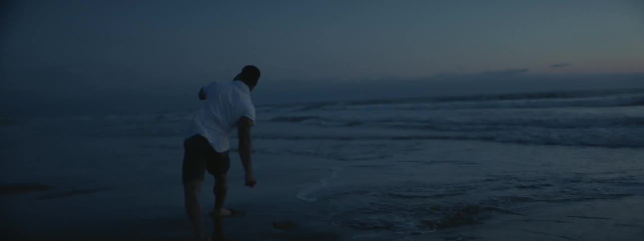 A man is practicing his fighting moves at the beach at dusk