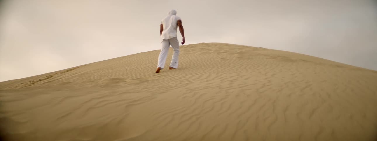A man is walking up a sand dune on a windy day