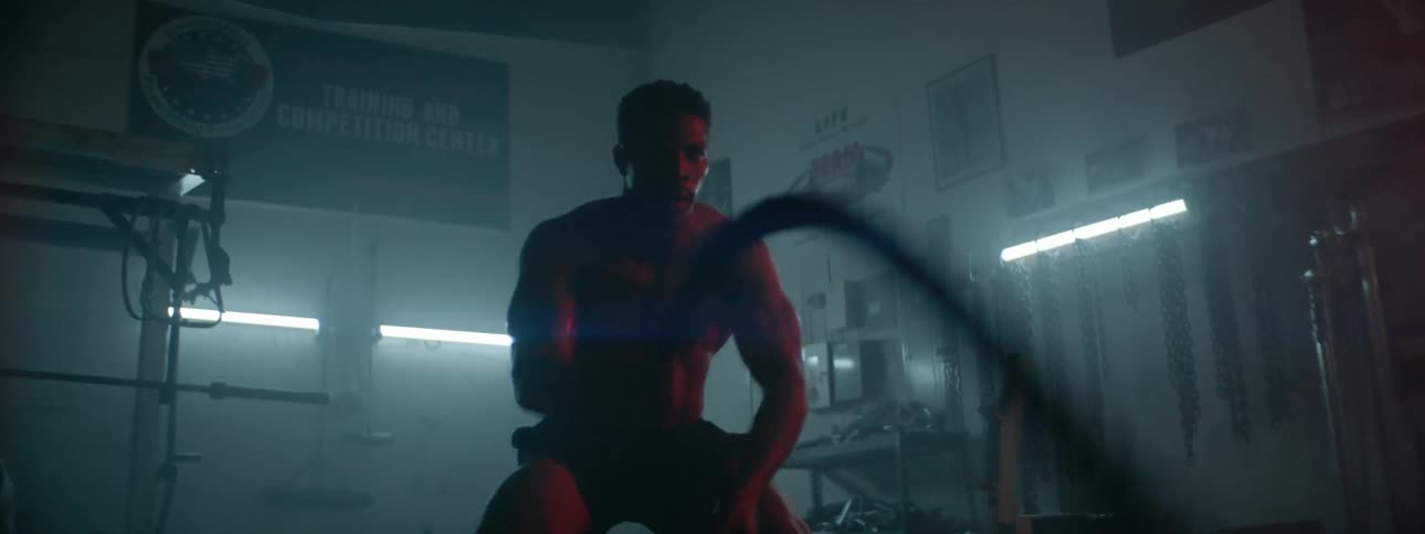 A sweaty man swings heavy ropes in a gym