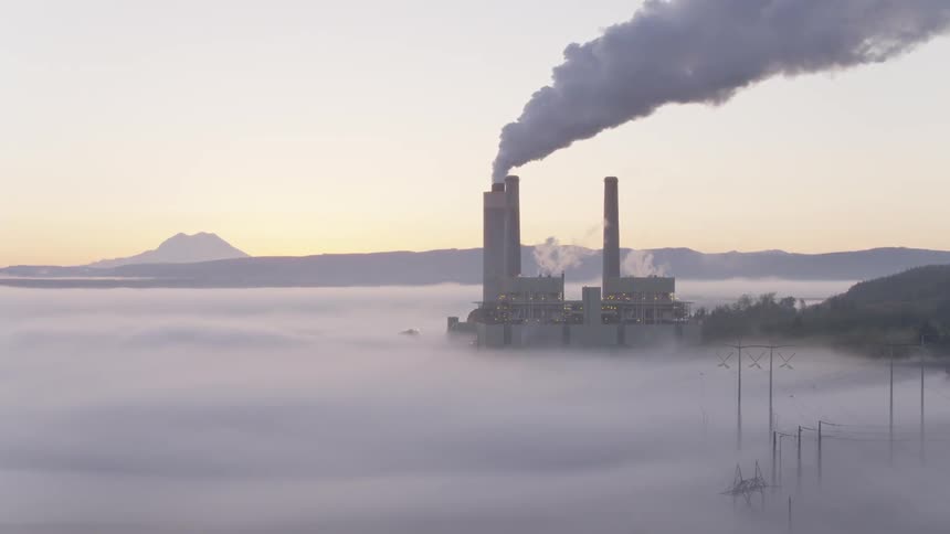 Slow orbit of a fossil fuel power station and transmission lines rising out of low fog along the ground