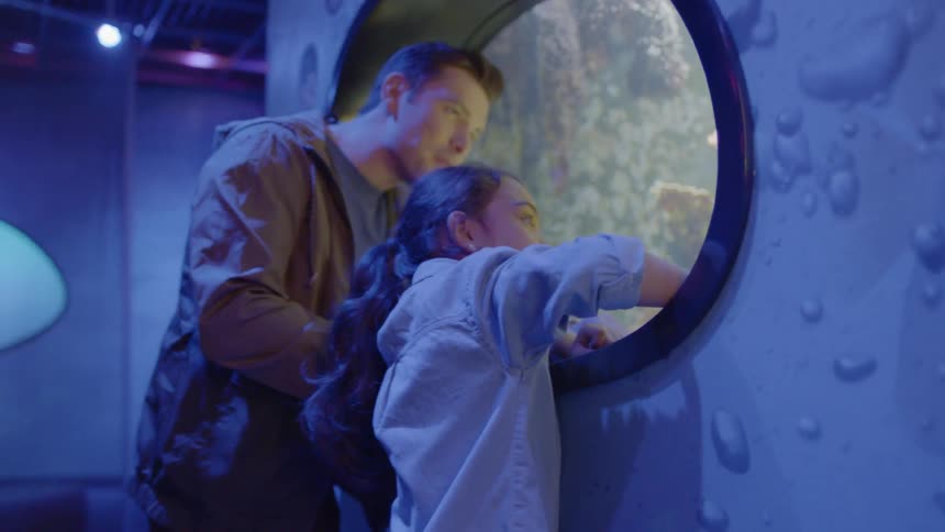 A girl with her dad looks through a round tank window in an aquarium