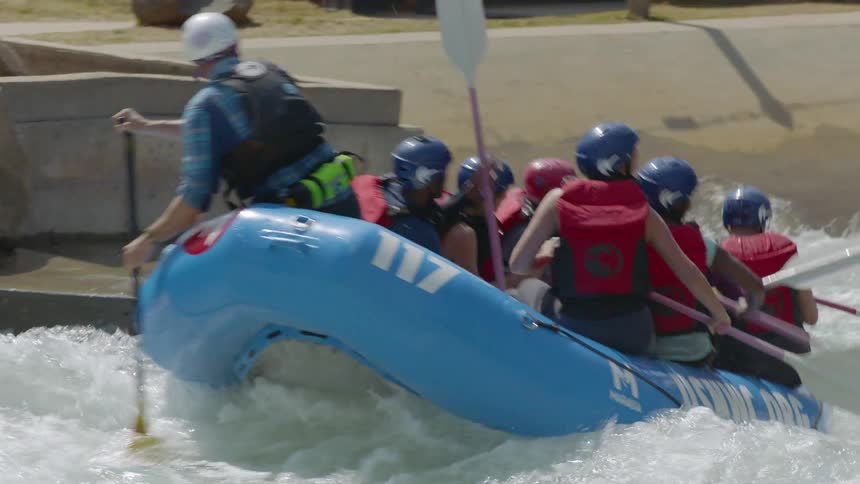 A group of people are in a paddle boat going over some white water rapids