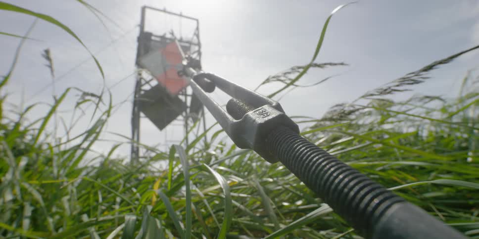 A cable secures a metal tower in a field