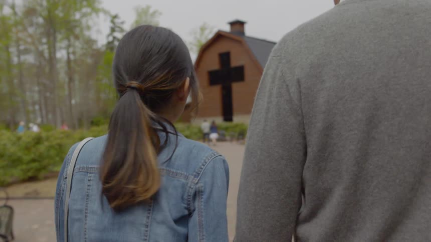 A man and woman are walking towards a large barn with a cross cut out of it