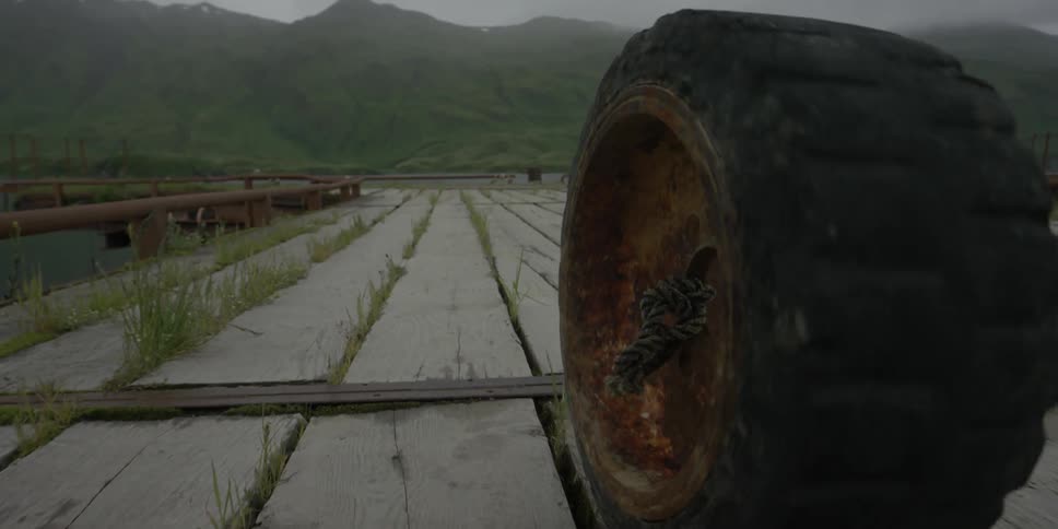 A large rusted tire rolls on wood boards