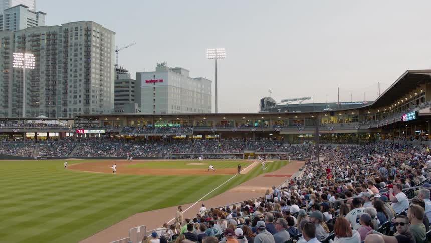 Spectators are watching a baseball game in a stadium at dusk
