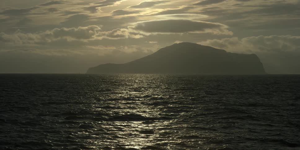 Ocean water ripples in front of an island on a cloudy day