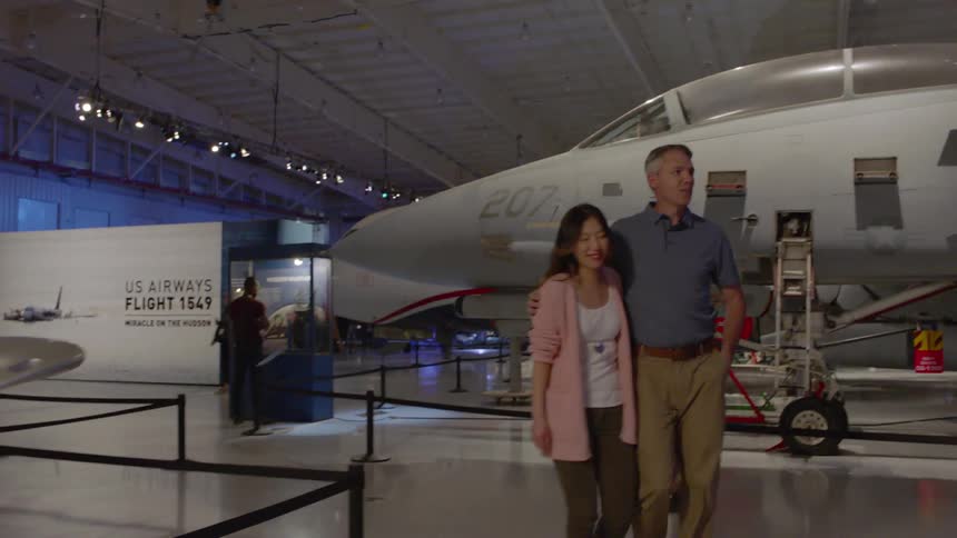 A couple hold each other as they are walking through an aerospace museum