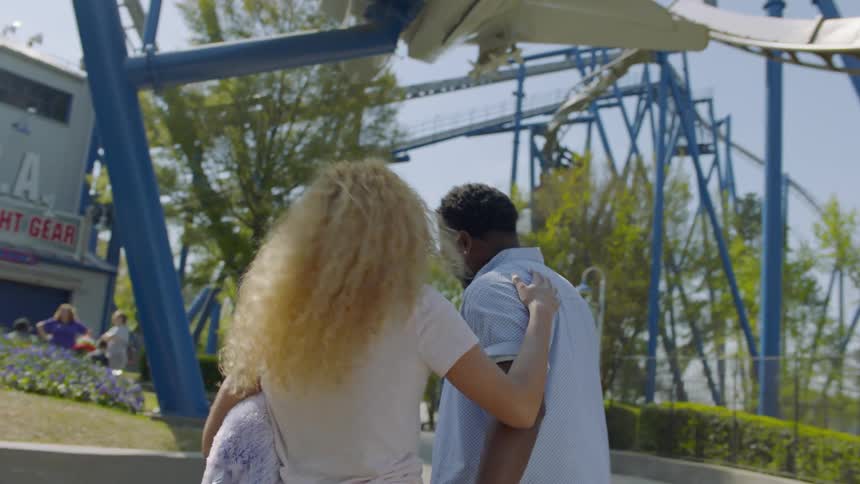 Man and woman hold hands and smile as they walk through an amusement park