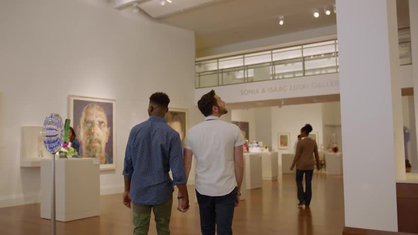 Two men hold hands walking in the museum