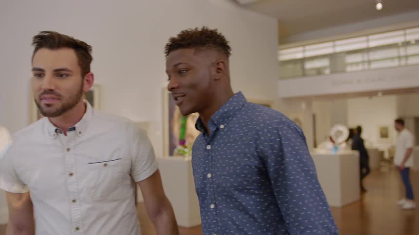 Two men hold hands while looking at an art exhibit