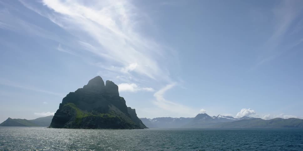 Clouds hover in the sky above a rock island on a sunny day