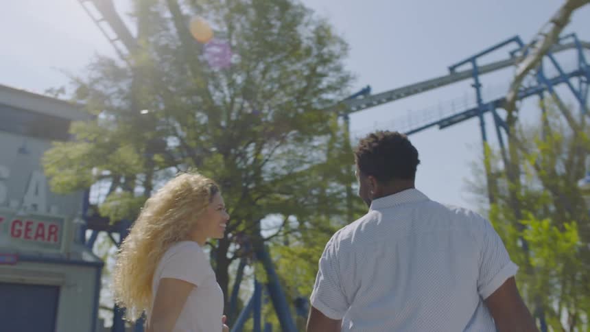 Man and woman walk by a roller coaster and woman points up smiling