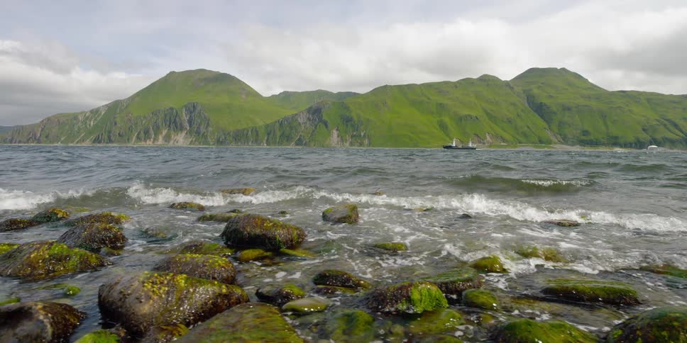 The waves are crashing against the green rocks