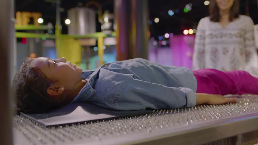 A girl lies on a bed of nails in an interactive museum