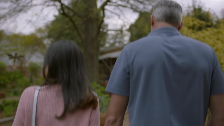A man and woman hold hands while walking in a garden