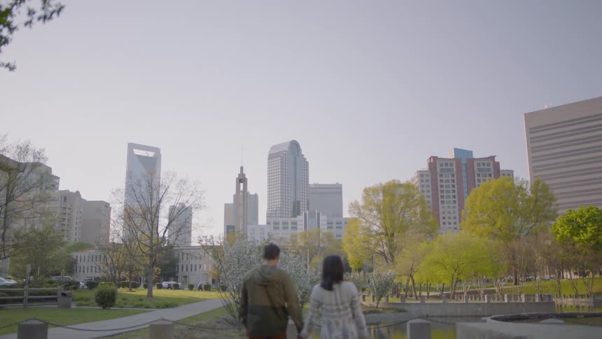 Man and woman hold hands while walking in a city park