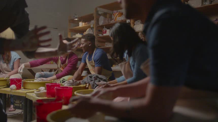 Several men and women make pottery together in a small room