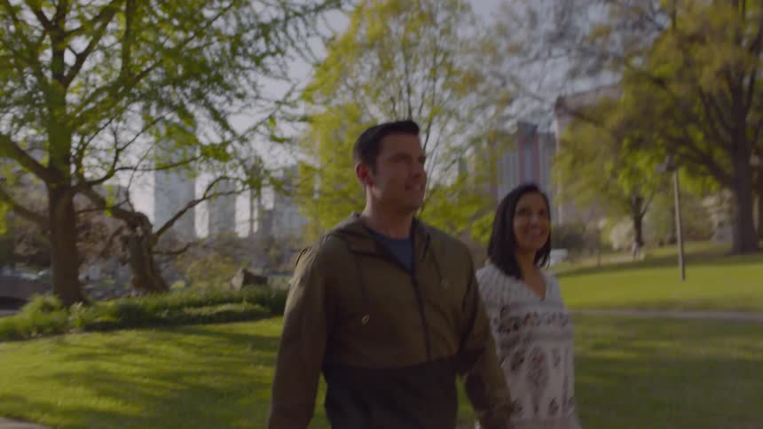 Man and woman hold hands while walking through a city park
