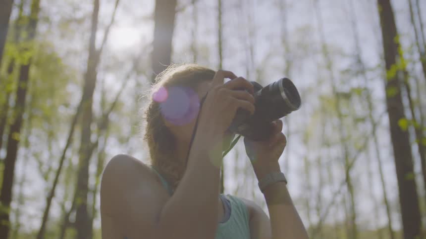 A woman looks around at the woods around her taking photos
