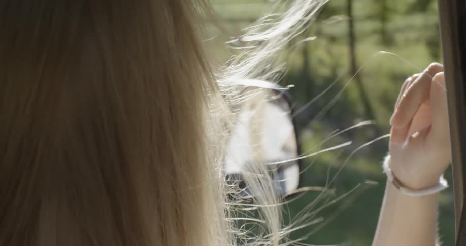 A woman's hair blows in the wind as she leans out the passenger window