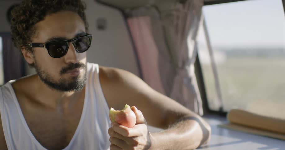 A man is sitting in the back of a van eating an apple