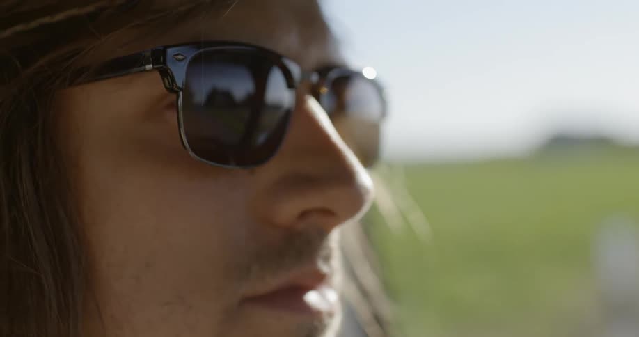 Man wearing sunglasses rides in a car on a sunny day