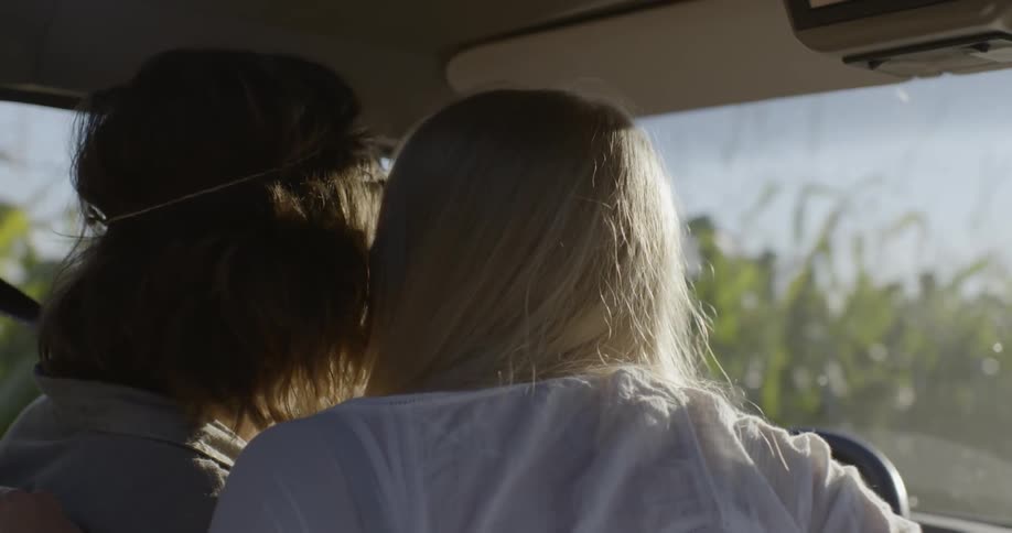 A man and a woman are driving next to a cornfield and the women leans over and kisses the man on the cheek