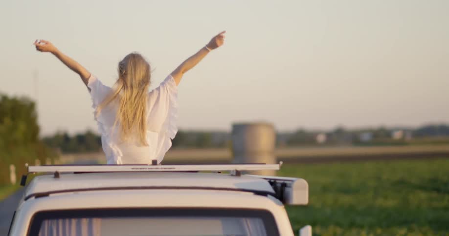 A woman rides in a truck raising her arms up