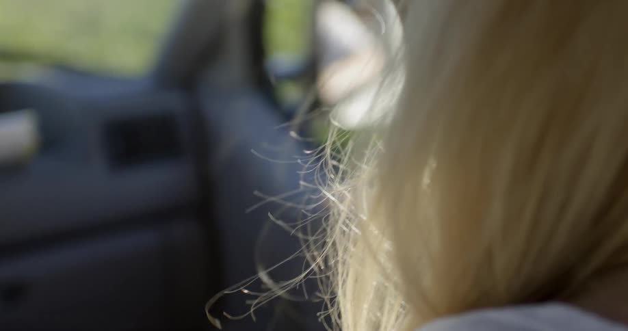 A woman with blonde hair is sitting in the passenger seat of a car