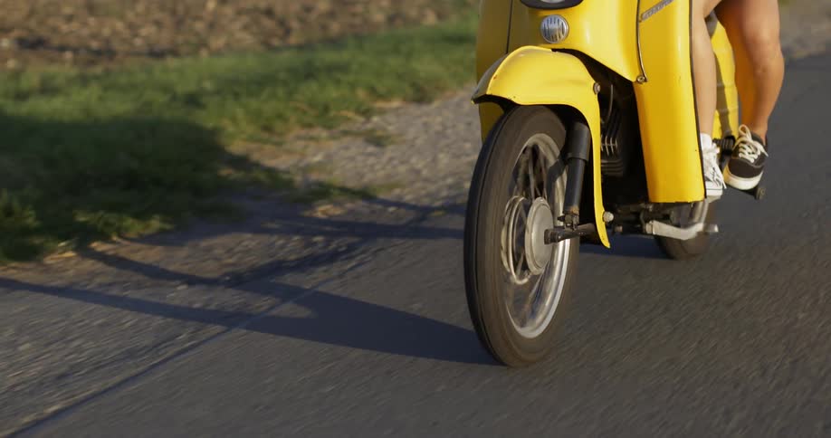 People ride on a yellow scooter