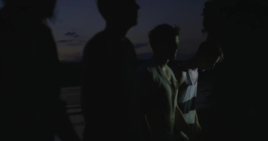 A group of men walk on the beach at night