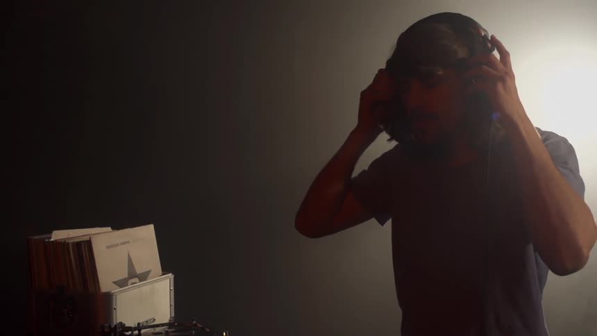 A man is putting on headphones as he stands in front of two turntables