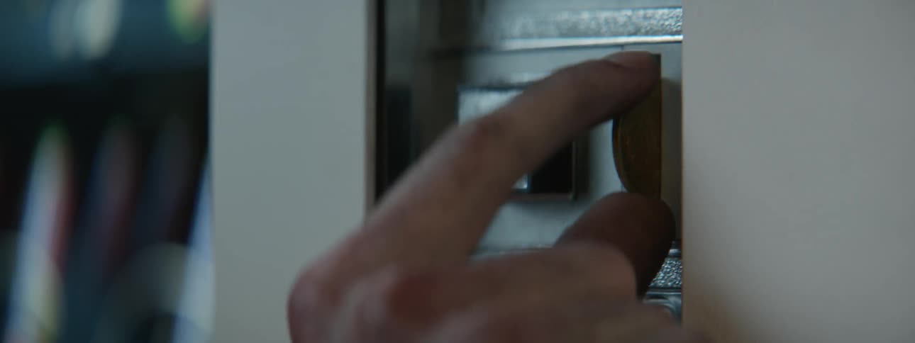 A person is putting a coin into a pay phone during the day