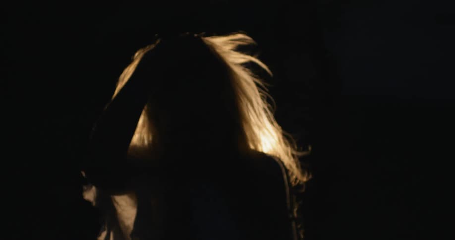 A woman walks in the night with a light shining behind her