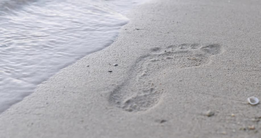 A footprint is in the sand of the beach