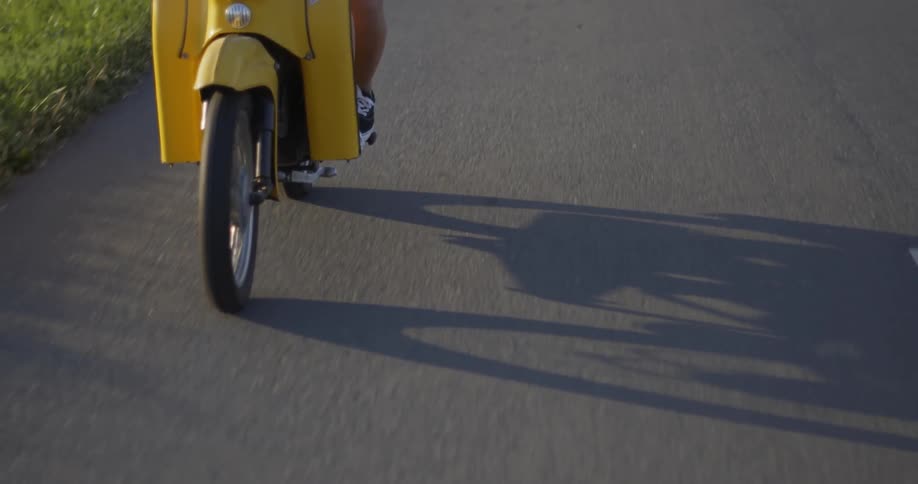 A yellow scooter rides on the road on a sunny day