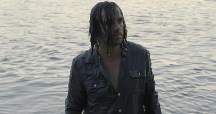 A man is soaking wet standing on the edge of a lake