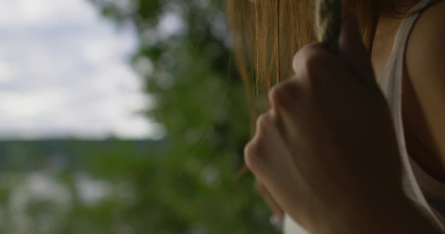 A teenage girl is sitting in a swing in a natural landscape at dusk