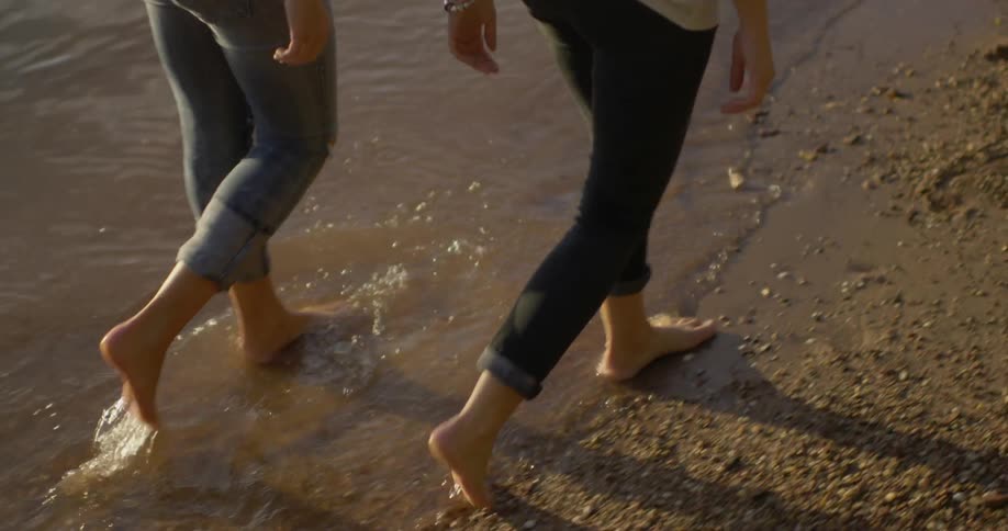 Two women walk in the sand by the water